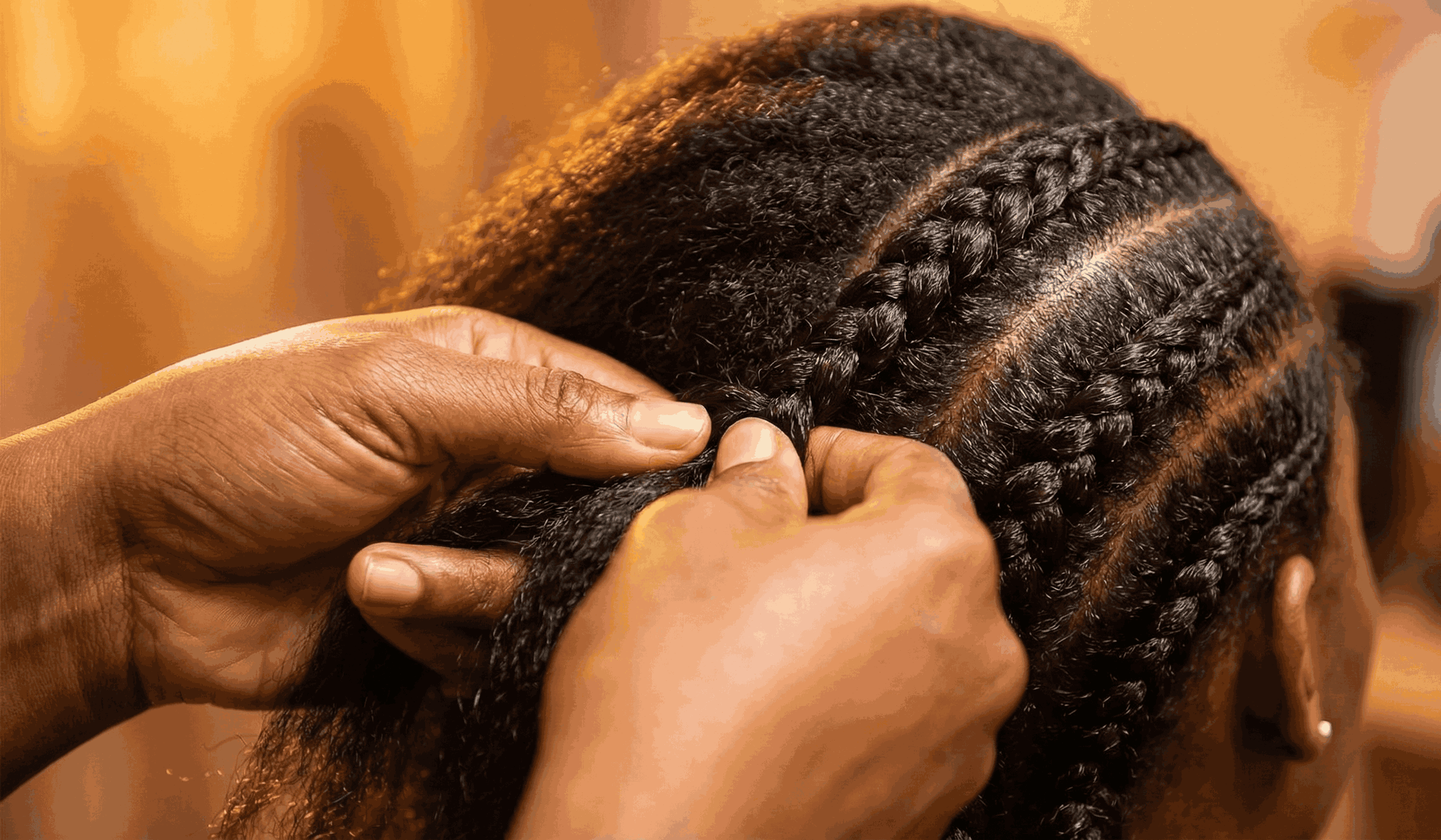 Close up of hands intricately braiding healthy hair, dramatic warm studio lighting
